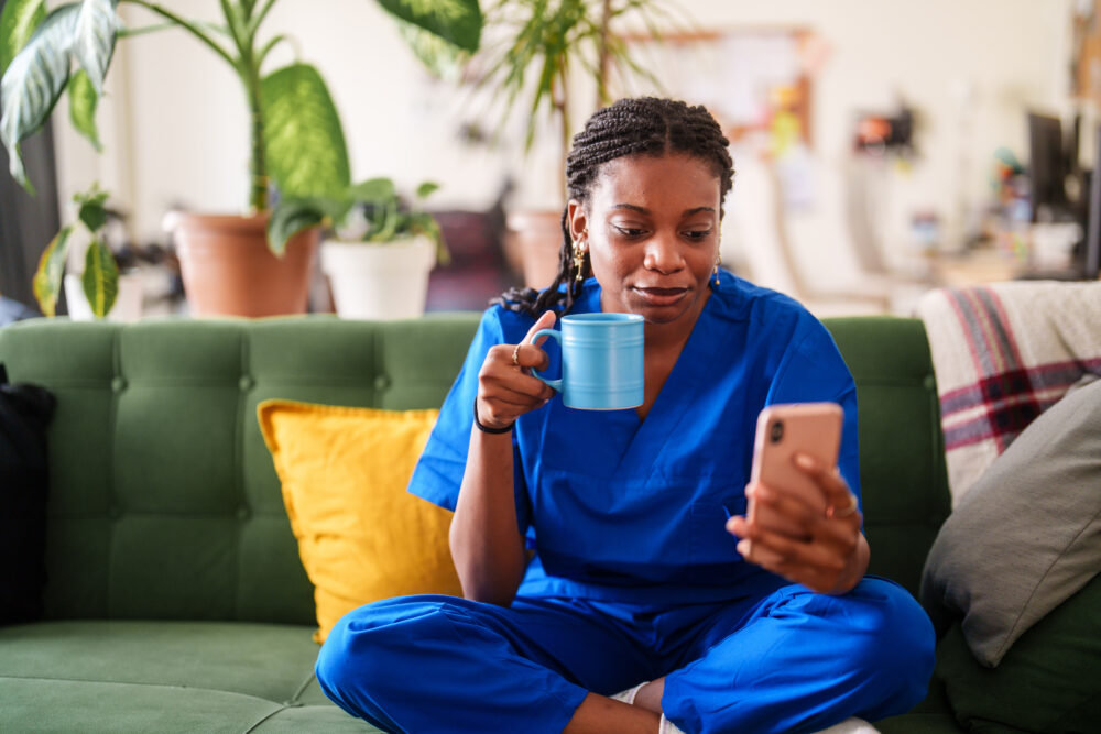 Woman in scrubs using mobile phone at home.
